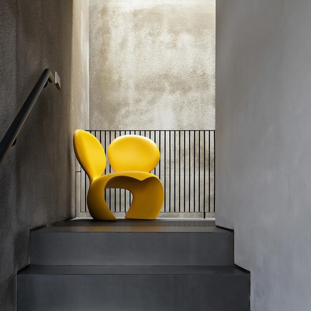 Don't F**k With The Mouse Yellow armchair on a staircase with a concrete wall and window by Qeeboo.