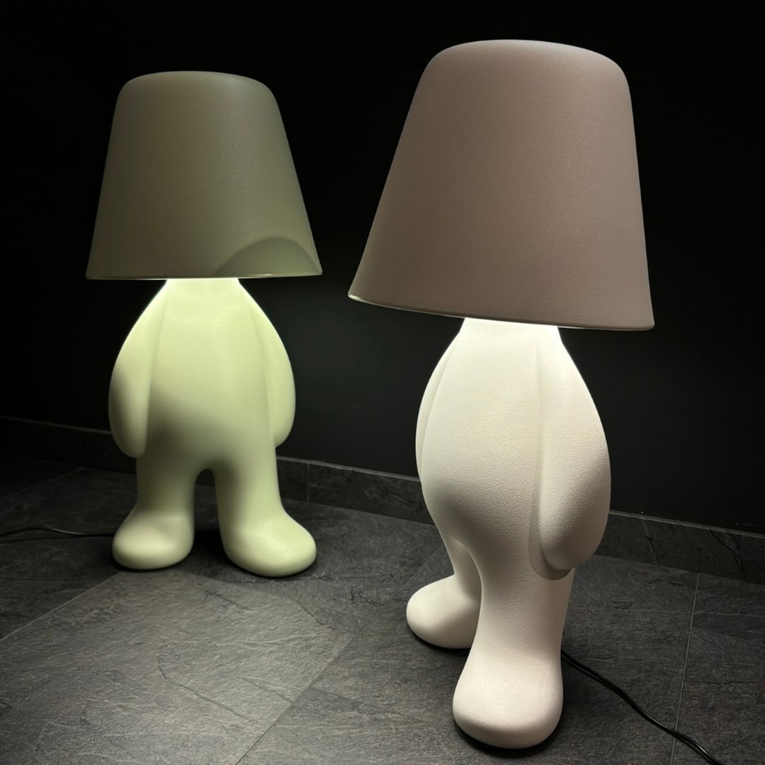 Qeeboo Bigger Brother Floor Lamps in green and white emitting soft ambient light, sculptural human‑shaped design on dark floor