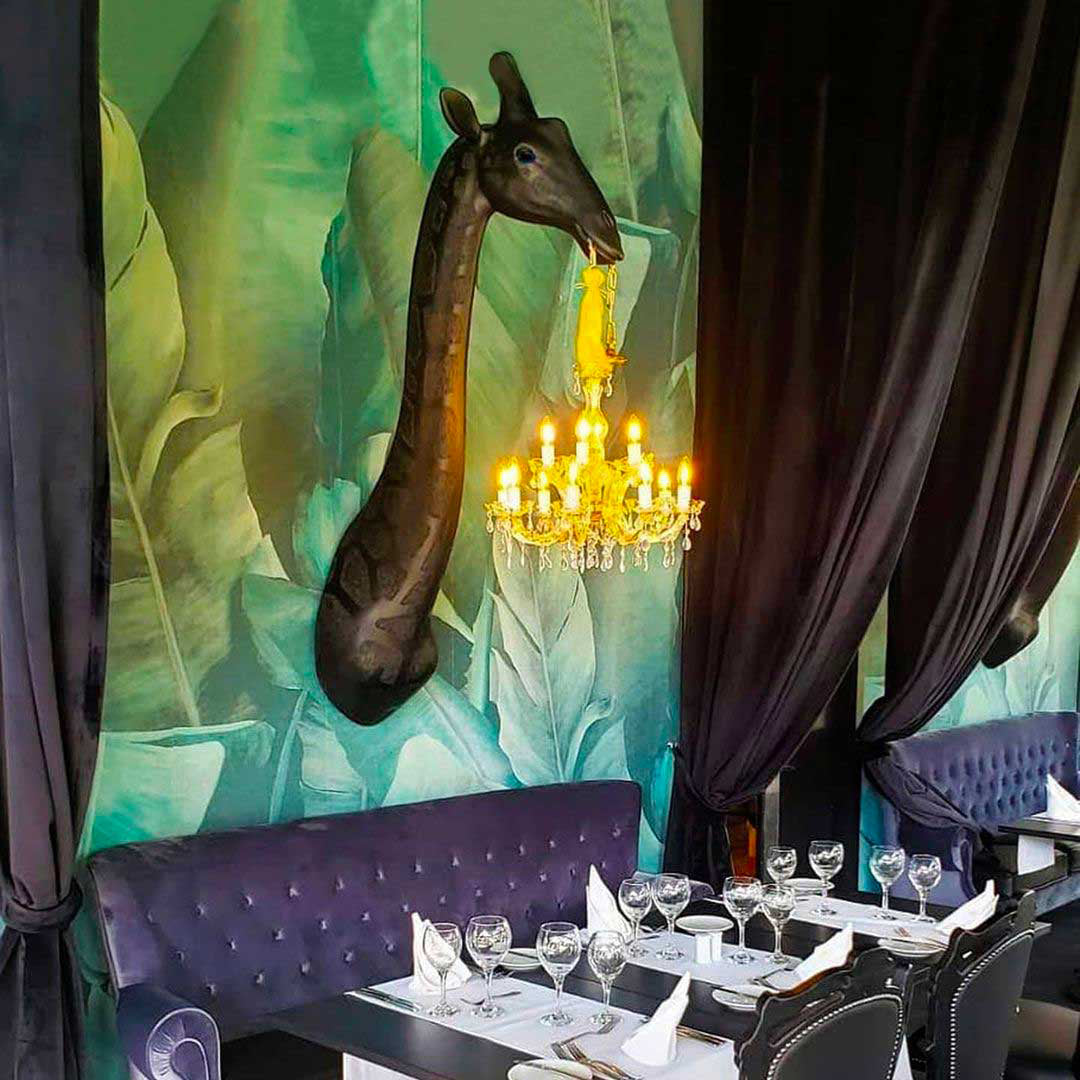 Restaurant dining area with a giraffe sculpture and chandelier by Qeeboo