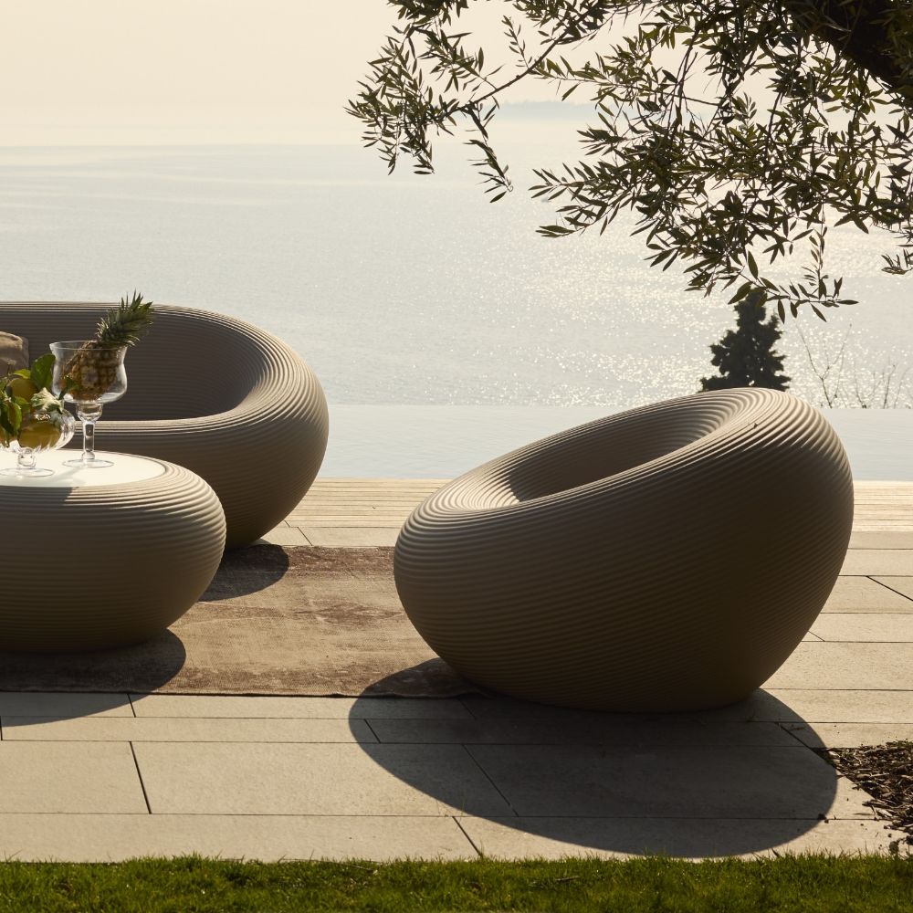 Qeeboo Nami outdoor armchairs and matching table with ribbed sculptural design in a serene lakefront patio setting