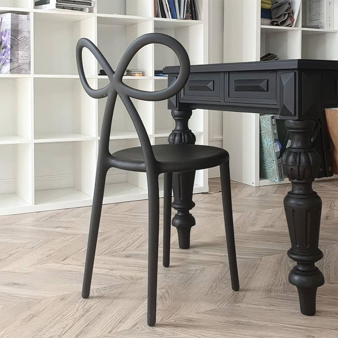 Qeeboo Black chair with unique back design in front of a dark wooden desk against a white bookshelf.