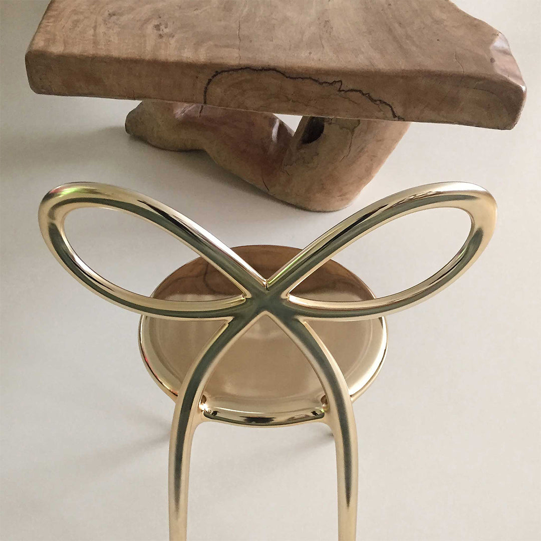 A modern side table featuring a polished gold-finished metal base with an infinity loop design and a round tray, Ribbon chair by Qeeboo